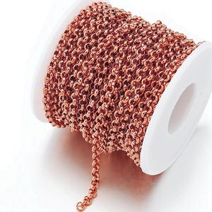 May include: A spool of rose gold colored chain, wound around a white plastic spool. The chain is a delicate, linked design.
