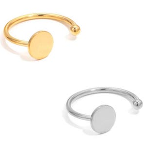 May include: Two open-ended rings. One is gold-toned, featuring a small, circular disc and a ball-shaped end. The other ring is silver-toned, with a similar design. Both rings are set against a white background.