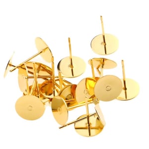 May include: A group of gold-colored earring posts with round backs. The posts are scattered on a white background.