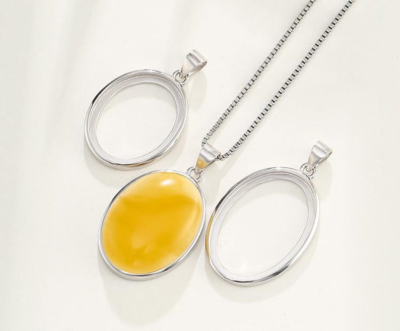 Puede incluir: Un collar de cadena de plata con tres colgantes ovalados. Dos de los colgantes est&aacute;n vac&iacute;os y un colgante presenta una piedra ovalada amarilla.