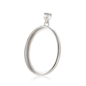 Puede incluir: Un colgante ovalado de plata con un acabado liso y pulido. El colgante tiene un aro en la parte superior para sujetar una cadena.