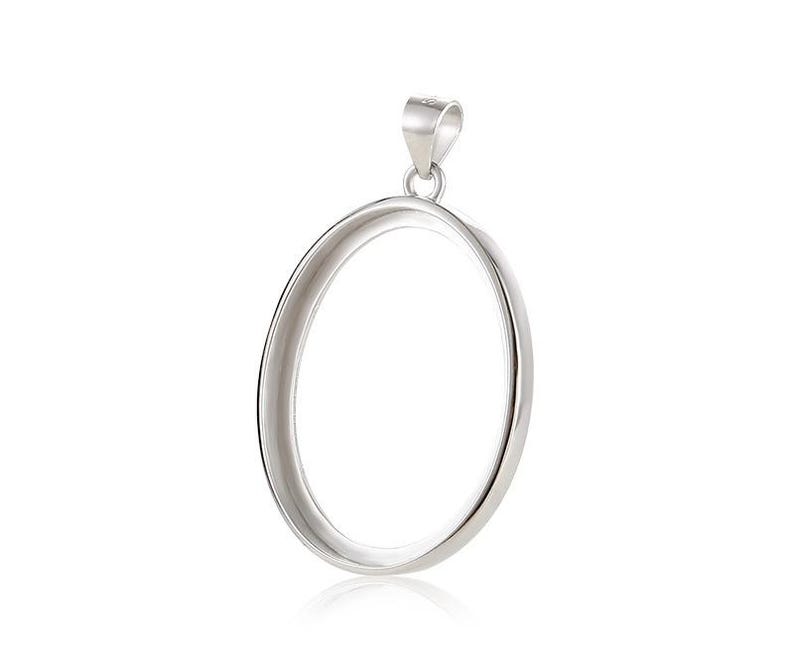 Puede incluir: Un colgante ovalado de plata con un acabado liso y pulido. El colgante tiene un aro en la parte superior para sujetar una cadena.