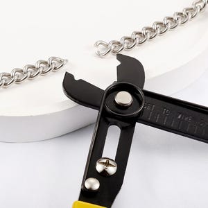 May include: A close-up of a black and yellow wire stripper tool beside a silver chain. The tool has a black handle and a yellow grip. The chain is made of interlocking metal links.
