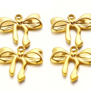 May include: Four gold-colored bow charms with a glossy finish. Each bow has a loop at the top for attaching to jewelry. The bows have a classic ribbon design with flowing tails, perfect for crafting earrings, necklaces, or bracelets.