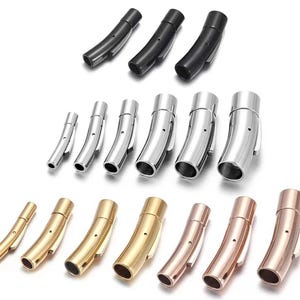 May include: An assortment of curved jewelry clasps in various metallic finishes, including black, silver, gold, and rose gold. The clasps are shown in multiple sizes, suitable for bracelets and necklaces. The clasps have a curved, tubular design with a secure closure mechanism.