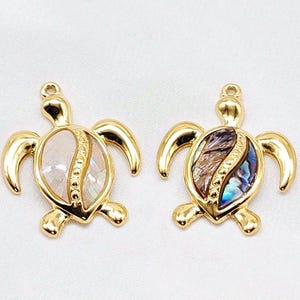 Può includere: Due ciondoli a forma di tartaruga dorati con intarsi di madreperla di abalone. Un ciondolo ha un intarsio di madreperla bianca e rosa, l'altro ha un intarsio di madreperla blu e verde.