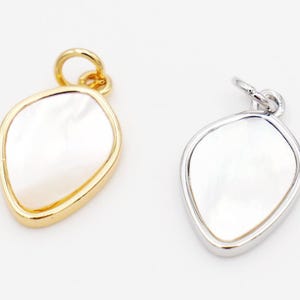 May include: Two pendant charms with a pearlescent inlay. One charm has a gold-tone bezel and bail, the other has a silver-tone bezel and bail. The charms have an irregular, organic shape, and are suitable for jewelry making.