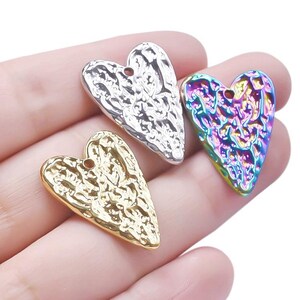 May include: Three heart-shaped metal charms with a textured surface. The charms are silver, gold, and iridescent.
