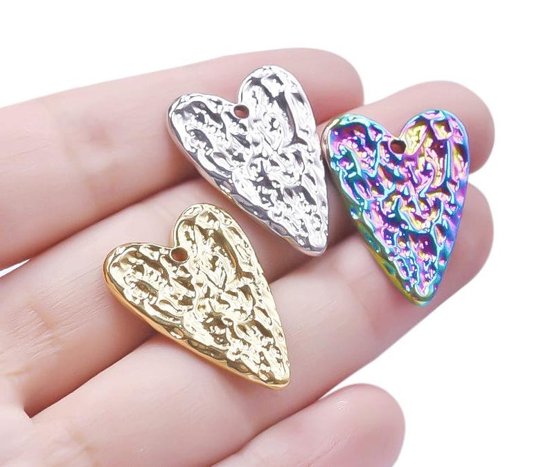 May include: Three heart-shaped metal charms with a textured surface. The charms are silver, gold, and iridescent.