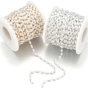 Peut inclure: Deux bobines de chaîne perlée. Une bobine présente des perles dorées, tandis que l'autre a des perles argentées. Les perles sont de forme ovale et enfilées ensemble. Les bobines sont blanches et le fond est blanc.