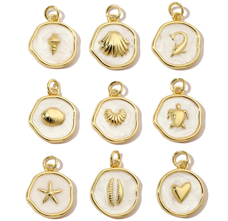 K&ouml;nnte beinhalten: Neun goldfarbene Anh&auml;nger mit wei&szlig;em Emaille, jeder mit einem anderen maritimen Design: eine Muschel, ein Seestern, ein Herz, ein Delfin, eine Schildkr&ouml;te, eine Venusmuschel, eine Jakobsmuschel, eine Welle und eine Muschel mit einer Perle.