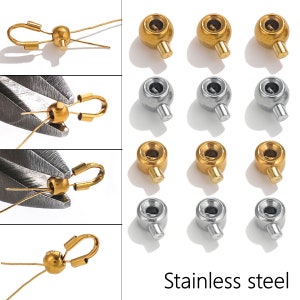 Könnte beinhalten: Nahaufnahme von goldenen und silbernen Metall-Quetschperlen. Die Perlen haben ein kleines Loch in der Mitte und eine kleine Schlaufe an der Seite. Die Perlen werden für die Schmuckherstellung verwendet.