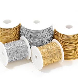 May include: Spools of metallic cord in gold and silver. The cord is tightly wound on white spools, with several spools visible. The cords have a shiny, reflective quality, suggesting they are made of metal or a metallic material. Ideal for jewelry making or crafting.