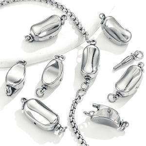 May include: A collection of shiny, silver-colored jewelry clasps and chain links. The clasps are oblong and have a smooth, reflective surface. The chain is made of small, interconnected links. The pieces are arranged on a white surface.