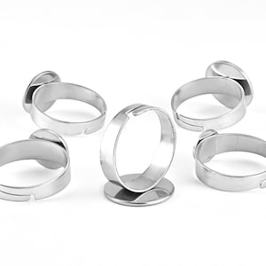 May include: Five silver rings with a round, flat, open space on the top, designed for adding a cabochon or other embellishment.