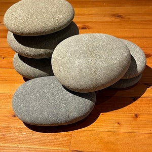May include: A stack of six smooth, gray and dark gray stones, arranged in a pyramid shape on a wooden surface.
