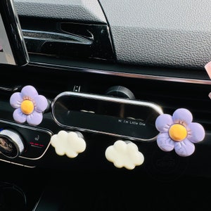 May include: Purple flower-shaped car air freshener with a yellow center and the text "Hi I'm Little One" on a black car air freshener holder.
