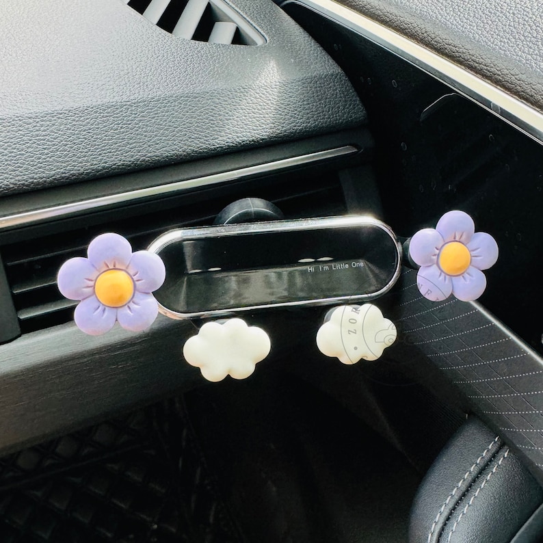 May include: A car phone holder with a purple flower, a white cloud, and a gray cloud with the text "Hi I'm Little One" on it.