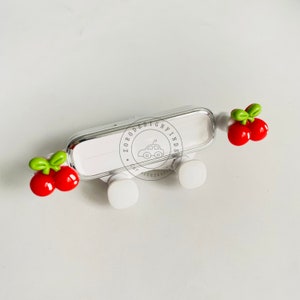 May include: A white car phone holder with a silver frame and red cherry accents. The holder has a rectangular shape with rounded corners and a clear plastic cover. The cherries have green stems and leaves. The text "ZORODESIGNFINDS" is printed on the holder.