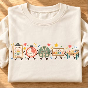 May include: A cream-colored long-sleeve shirt featuring a graphic print of five anthropomorphic items: a clipboard with a checklist, a red timer, a green cardigan, a rectangular box with colorful circles, and a small table with geometric shapes.