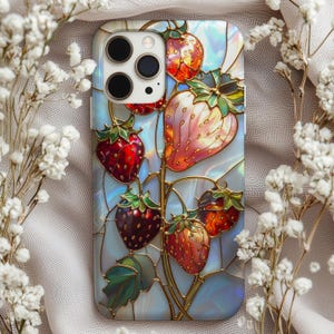 Puede incluir: Funda de teléfono con diseño de vidriera de fresas. El diseño presenta fresas rojas y rosas con hojas verdes, contorneadas en dorado, sobre un fondo nacarado. Las lentes de la cámara del teléfono son visibles en la parte superior.