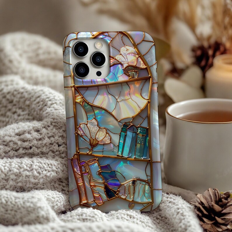 Peut inclure: Coque de smartphone avec un motif de vitrail. L'&eacute;tui pr&eacute;sente un fond nacr&eacute; avec des contours dor&eacute;s et des formes abstraites color&eacute;es. Le motif comprend des &eacute;l&eacute;ments floraux et g&eacute;om&eacute;triques dans des tons de bleu, de violet et d'or.
