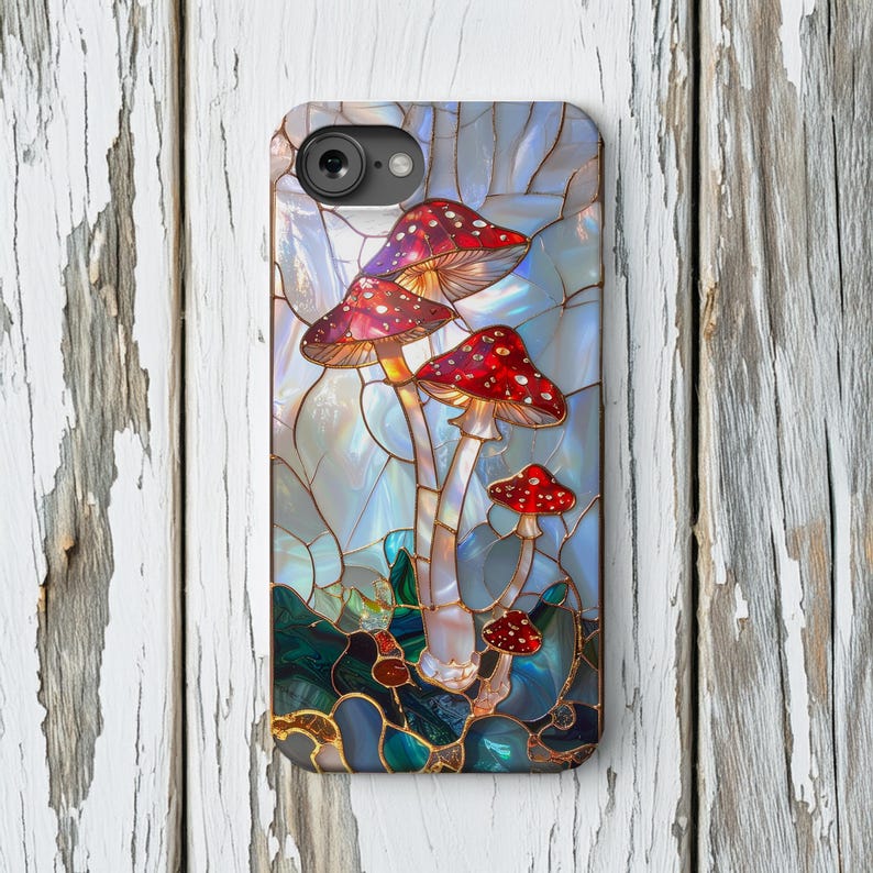 K&ouml;nnte beinhalten: Handyh&uuml;lle mit einem Buntglas-Design von rot-wei&szlig; gepunkteten Pilzen. Die Pilze haben ein detailliertes, k&uuml;nstlerisches Aussehen vor einem blau-gr&uuml;nen Hintergrund. Die H&uuml;lle hat eine gl&auml;nzende Oberfl&auml;che.