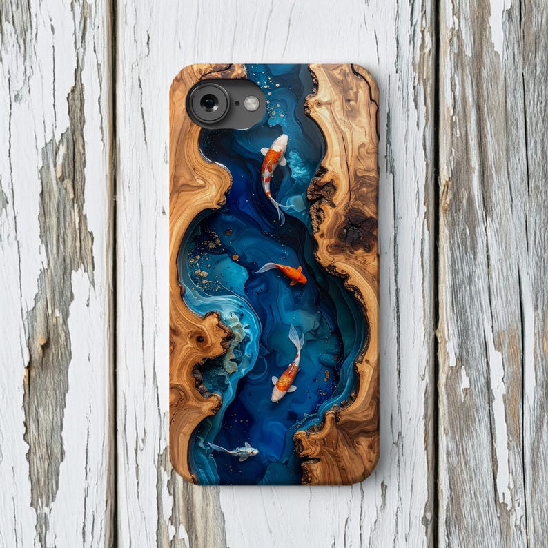 Op de afbeelding: Telefoonhoesje met een uniek ontwerp van een blauwe rivier met koi-vissen. De hoes is gemaakt van hout en hars, met een natuurlijke houtnerf rand. De koi-vissen zijn oranje en wit.