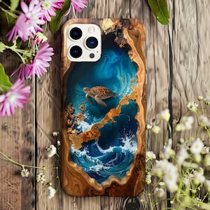 以下が含まれることがあります： 青い水と白い波の中で泳ぐウミガメのデザインが施された木製の携帯電話ケース。ケースは天然の木目模様の縁と金のアクセントが付いています。デザインは芸術的で、自然をテーマにしています。