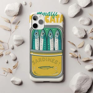 May include: A white phone case featuring a sardine can design. The can is yellow with the word "SARDINES" and a fish illustration. Four fish are inside the can, with the text "#malfi CATA" at the top. The case has a camera cutout.