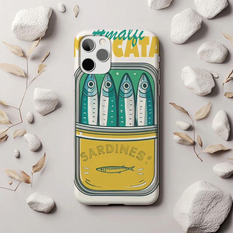 May include: A white phone case featuring a sardine can design. The can is yellow with the word "SARDINES" and a fish illustration. Four fish are inside the can, with the text "#malfi CATA" at the top. The case has a camera cutout.