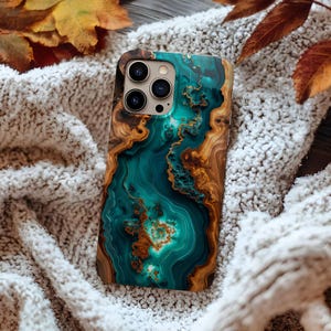 Puede incluir: Una funda de teléfono inteligente con un diseño único que presenta un patrón veteado turquesa y marrón. La funda tiene un acabado brillante y un recorte para la cámara. Descansa sobre una superficie blanca texturizada con hojas de otoño en el fondo.