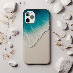 May include: A phone case with a beach design. The top half shows turquoise ocean waves with white foam, leading to a sandy beige base. The case has a dark blue border and a camera cutout.