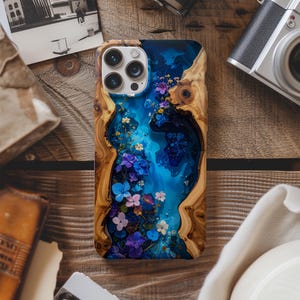 May include: A wooden phone case with a blue resin river design, adorned with colorful flowers. The case has a natural wood grain border and a glossy finish, creating a unique and artistic look. The case is designed for a smartphone with multiple camera lenses.