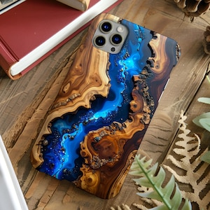 May include: A wooden phone case with a blue resin river design. The case features a natural wood grain pattern with a vibrant blue and dark blue resin inlay. The case has a camera cutout and is on a wooden surface.