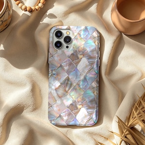 Könnte beinhalten: Eine perlmuttfarbene Handyhülle mit einem gewebten, mosaikartigen Design. Die Hülle hat ein quadratisches Muster mit schillernden Farben, darunter Weiß, Rosa und Blau. Die Handyhülle hat einen Kameraausschnitt und ist von einem silbernen Rahmen umgeben.