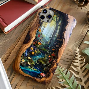 May include: A rectangular phone case featuring a wood grain border surrounding a central illustration of a lush forest scene with a blue stream, colorful wildflowers, green moss, and red mushrooms under tall trees with a triple camera cutout.
