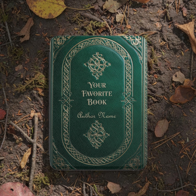 May include: A hardcover book with a dark green cover and gold embossed detailing. The text "YOUR FAVORITE BOOK" and "Author Name" are displayed on the cover. The book is lying on a bed of leaves and soil.