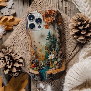 May include: A smartphone case featuring a detailed forest scene with a flowing blue stream, tall evergreen trees, and colourful autumn foliage. The design includes white daisies, small brown acorns, and textured bark elements, creating a layered woodland landscape.