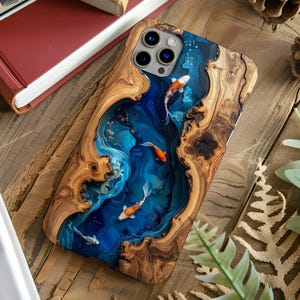 May include: A wooden phone case featuring a blue resin river design with koi fish. The case has a natural wood grain border and a glossy finish. The koi fish are orange and white, swimming in the blue resin river.