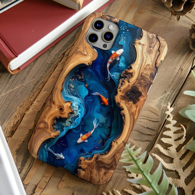Op de afbeelding: Houten telefoonhoesje met een blauwe hars rivier ontwerp en koi karpers. De hoes heeft een natuurlijke houtnerf rand en een glanzende afwerking. De koi karpers zijn oranje en wit.