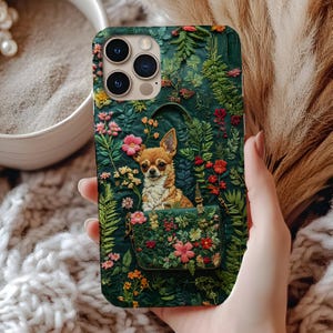 May include: A phone case with a detailed illustration of a Chihuahua dog in a floral handbag, set against a backdrop of lush green foliage and colourful flowers. The case has a dark green base with a textured appearance.
