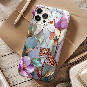 May include: A smartphone case featuring a stained-glass design with a leopard and floral elements. The case has a pearlescent background with purple, green, and orange accents. The leopard has a spotted coat and is surrounded by stylized leaves and flowers.
