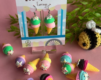 May include: A set of handmade ice cream cone earrings. The earrings are made of polymer clay and feature different colors and sprinkles. The earrings are on a pink background with a sign that says "Ice Cream Earrings".
