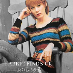 May include: A vintage knitting pattern cover featuring a woman in a striped sweater. The sweater has horizontal stripes in black, blue, brown, and tan. The text "FABRIC FINDS UK vintage KNITTING PATTERN" is visible.