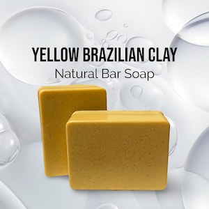 May include: Two bars of yellow Brazilian clay soap. The soap is natural and has a rough texture. The soap is on a white background with water droplets.