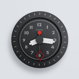 May include: A round, black wall clock with white numerals and hands. The second hand and a dot at the 12 o'clock position are red. The word "vone." is printed above the centre. The clock has a minimalist design and is suitable for any room.