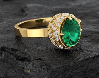 May include: A gold ring with a large oval emerald gemstone. The ring's setting is encrusted with small, sparkling diamonds. The band is smooth and polished, and the ring is displayed on a dark, textured surface.