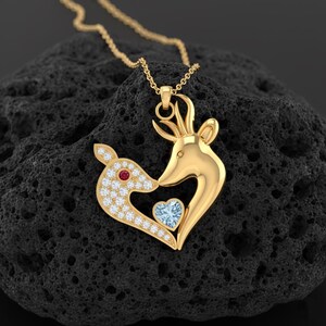 May include: A gold pendant necklace with a deer design. One deer is encrusted with small white stones and a red stone eye, while the other deer has a blue heart-shaped stone. The necklace is on a gold chain.