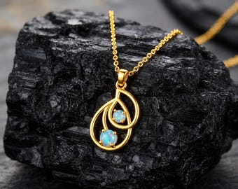 May include: A gold necklace featuring a pendant with two interlocking teardrop-shaped loops. Each loop contains a small, round, iridescent opal gemstone. The pendant is suspended from a delicate gold chain, showcasing a polished metallic finish.